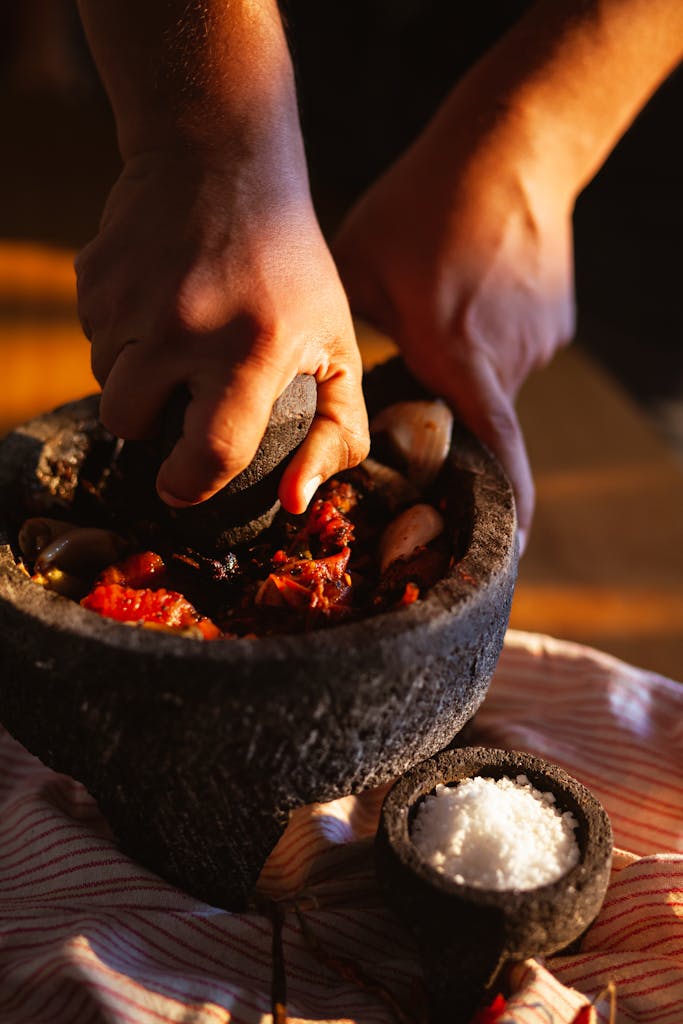 Close-up of hands using a mortar and pestle to crush ingredients for traditional Mexican cuisine.