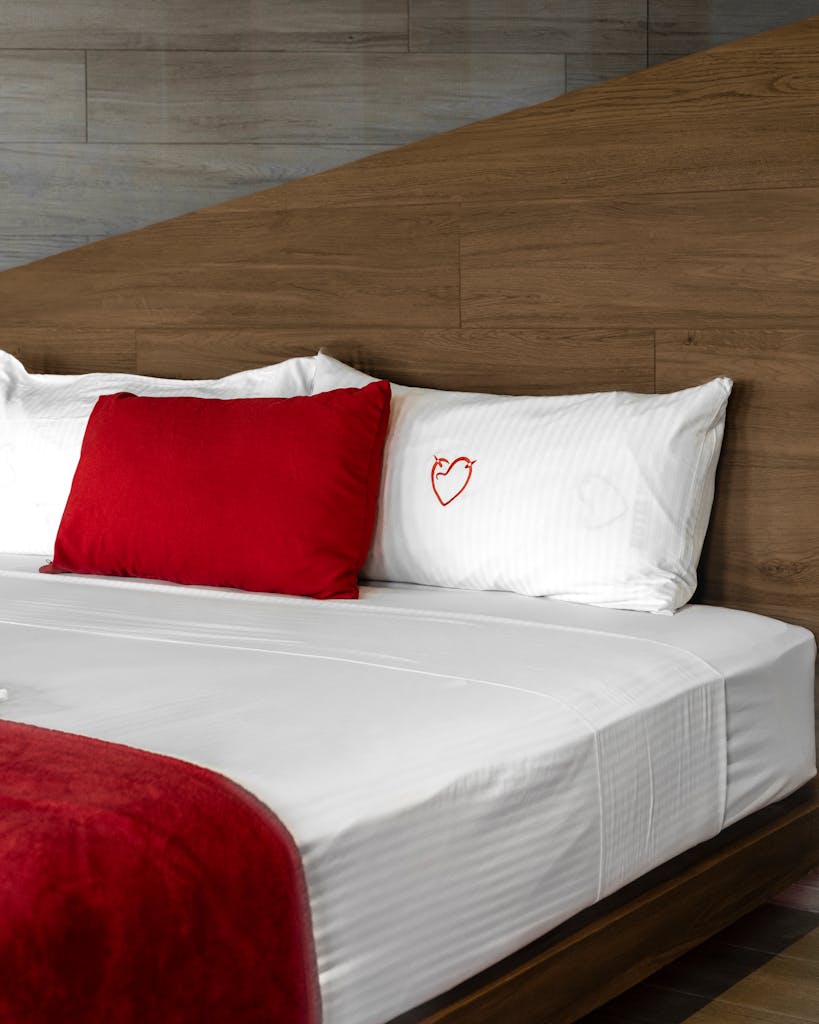 Contemporary hotel room interior featuring a cozy bed with red accents and heart embroidery in Ciudad de México.